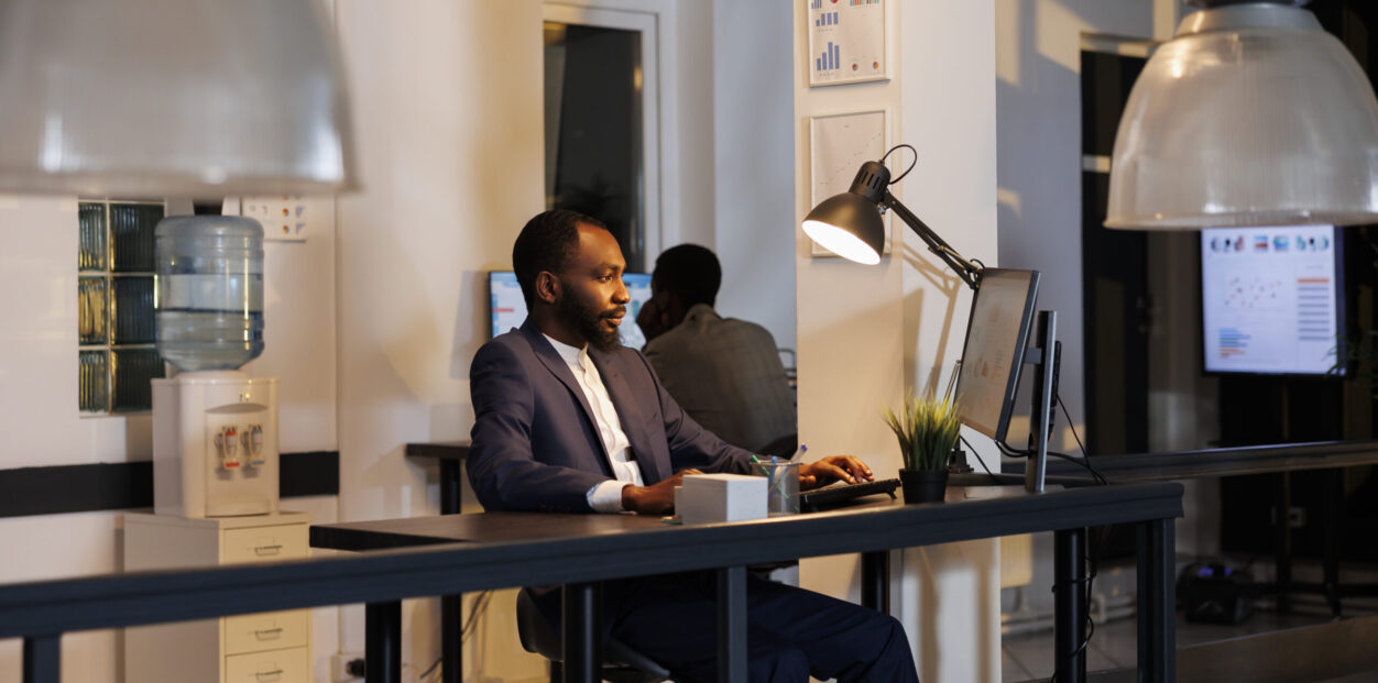 Entrepreneur analyzing marketing statistics working at financial growth report over hours in startup office. African american workers planning company strategy to increase business profit