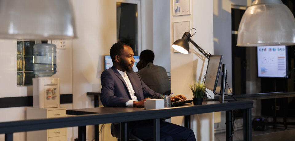 Entrepreneur analyzing marketing statistics working at financial growth report over hours in startup office. African american workers planning company strategy to increase business profit